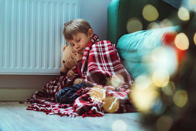 Cute little boy wrapped id plaid sitting by heater