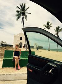 Beautiful woman sitting by church at beach seen through car