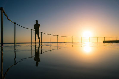 Shirtless man walking by railing in infinity pool during sunset
