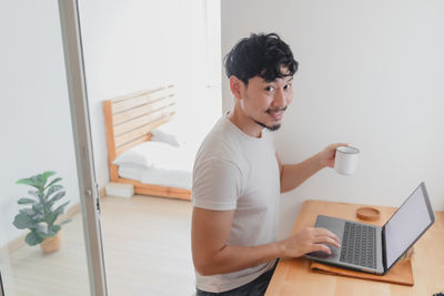 Side view of young man using laptop at home