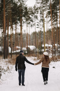 A happy couple in love in winter clothes hugging together walking in a snowy forest on an weekend