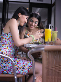 Cheerful friends using mobile phone while sitting at restaurant