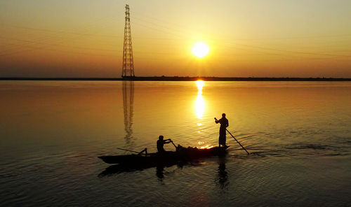 Silhouette men oaring fishing boat in river during sunset