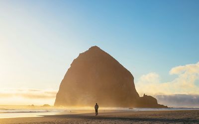 Man walking at beach against mountain and sky during sunrise