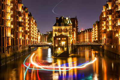 Illuminated bridge over river amidst buildings in city at night