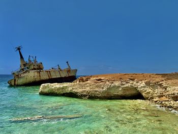 Scenic view of sea, with shipwreck against clear blue sky