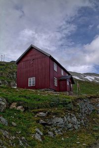 House on grassy field against cloudy sky