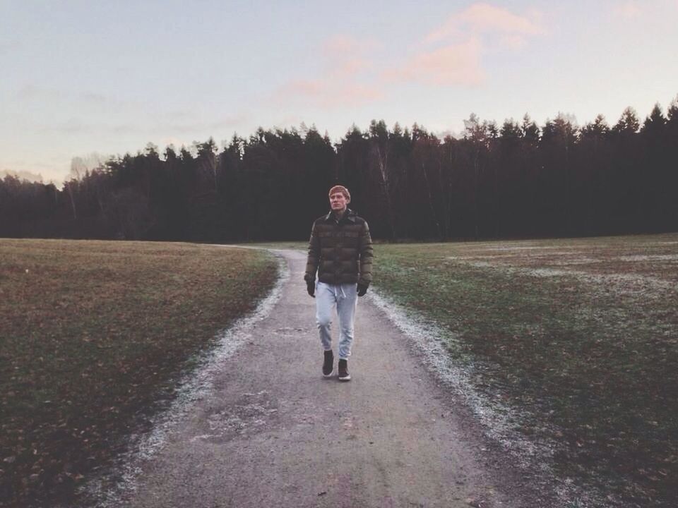 full length, lifestyles, tree, the way forward, rear view, walking, leisure activity, casual clothing, road, standing, sky, field, front view, dirt road, nature, landscape, tranquil scene, outdoors