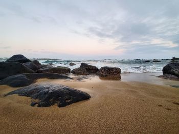 Rocks on beach against sky during sunset