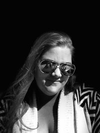 Close-up portrait of young woman wearing sunglasses against black background