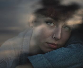 Close-up portrait of young woman seen through window during sunset