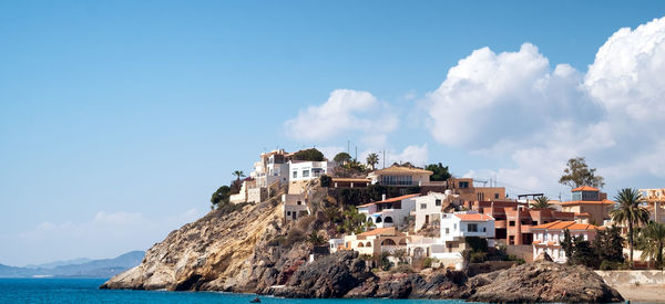 Town on rock formation in sea against sky