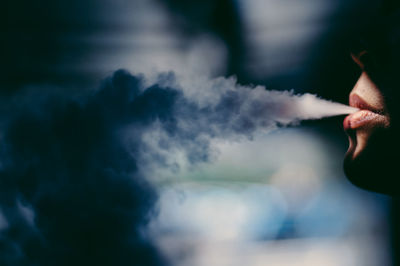 Cropped image of woman blowing smoke