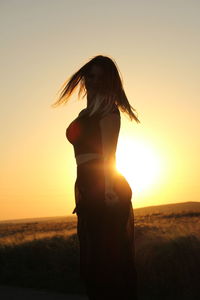Silhouette mature woman shaking head while standing on field against clear sky at sunset
