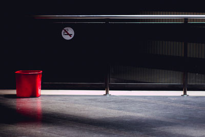 Red garbage can against no smoking sign on wall