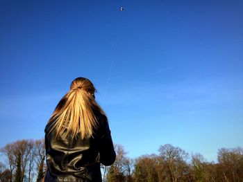 Rear view of woman with blond hair against blue sky