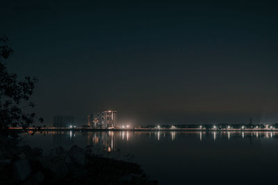 Illuminated city by lake against sky at night