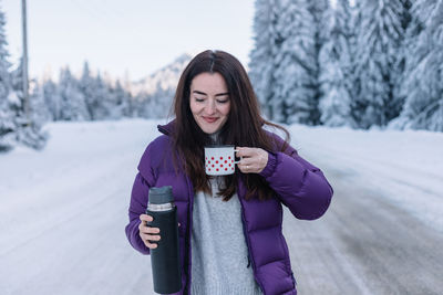 Portrait of smiling young woman standing on snow covered field