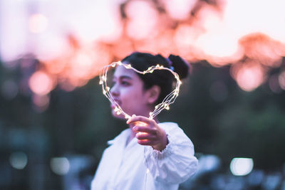 Side view of young woman holding string light