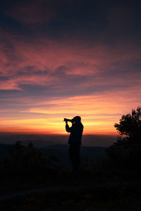 Silhouette man standing against orange sky during sunset