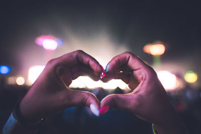 Cropped hands of woman making heart shape at night