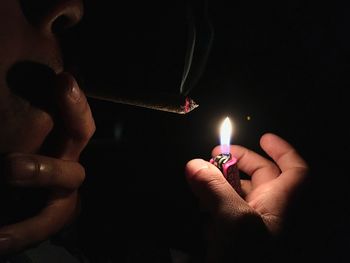 Cropped image of man lighting cigarette with lighter in dark