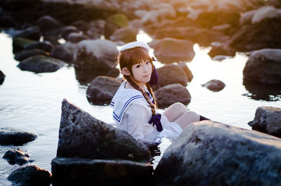 Rear view of woman sitting on rock at shore