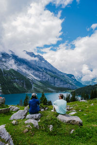 Rear view of people sitting on mountain against sky