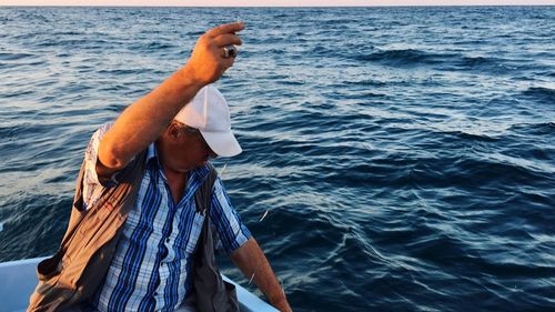 Man sitting on boat while fishing in sea