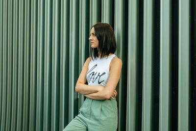 Thoughtful young woman looking away while standing against corrugated iron