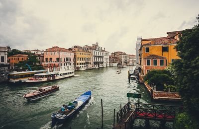 Boats in canal amidst cityscape against sky