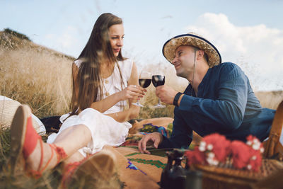 Couple holding wine in glasses while sitting on land against sky