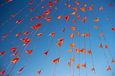 Low angle view of orange buntings against clear blue sky