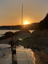 Woman with dog walking at beach during sunset