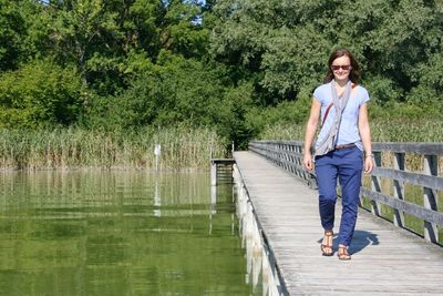 Full length of woman walking on pier over lake against trees