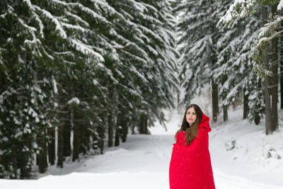 Woman wearing red hooded cloak amidst trees on snowy field