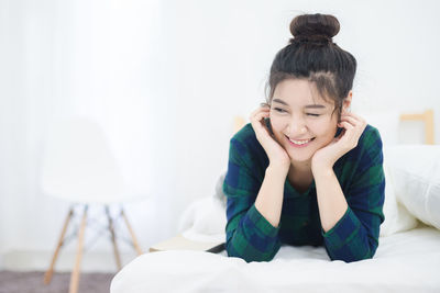 Smiling young woman winking while lying on bed at home