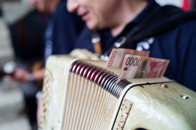 Midsection of man holding accordion with paper currency