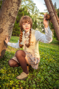 Full length of young woman crouching by tree outdoors