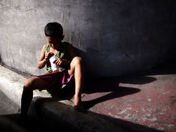 Full length of boy sitting on concrete wall