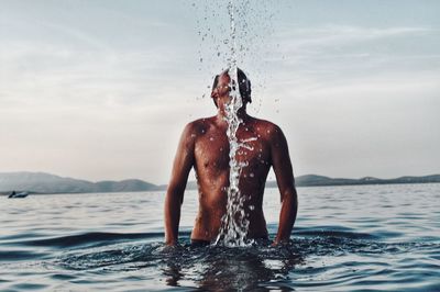 Shirtless man splashing water in sea against sky