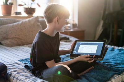 Young person showing art done on tablet computer while sitting on bed