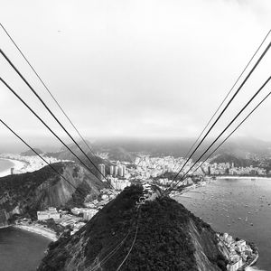 Steel cables over sugarloaf mountain in sea against cloudy sky