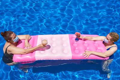 Two women bathe in a pool with a sanitary mask. they maintain the safety distance.