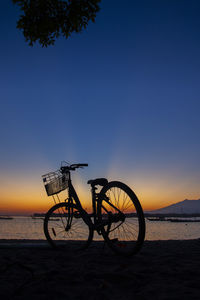 Silhouette bicycle at beach against sky during sunset