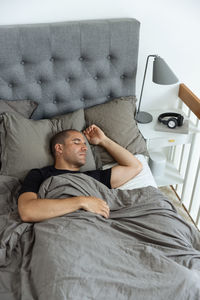 From above of peaceful male lying in soft bed under blanket and sleeping in morning in bedroom