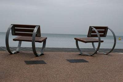 Empty chairs on beach against sky