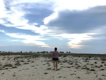 Rear view of woman walking at beach against cloudy sky during sunset