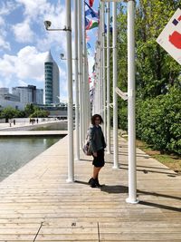 Full length of woman standing on boardwalk by river in city