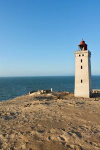 Lighthouse on beach against clear blue sky